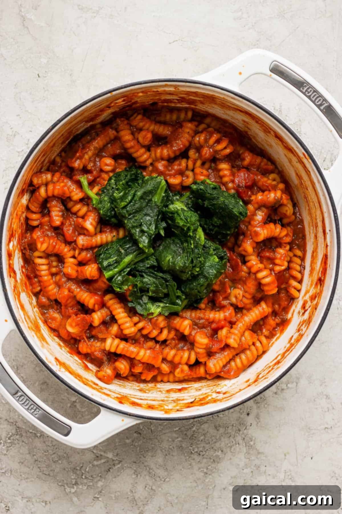 One-Pot Wonder Vodka Pasta 5 A white ceramic pot filled with rich tomato sauce and pasta, with wilted spinach mixed in, steaming gently on the stove.