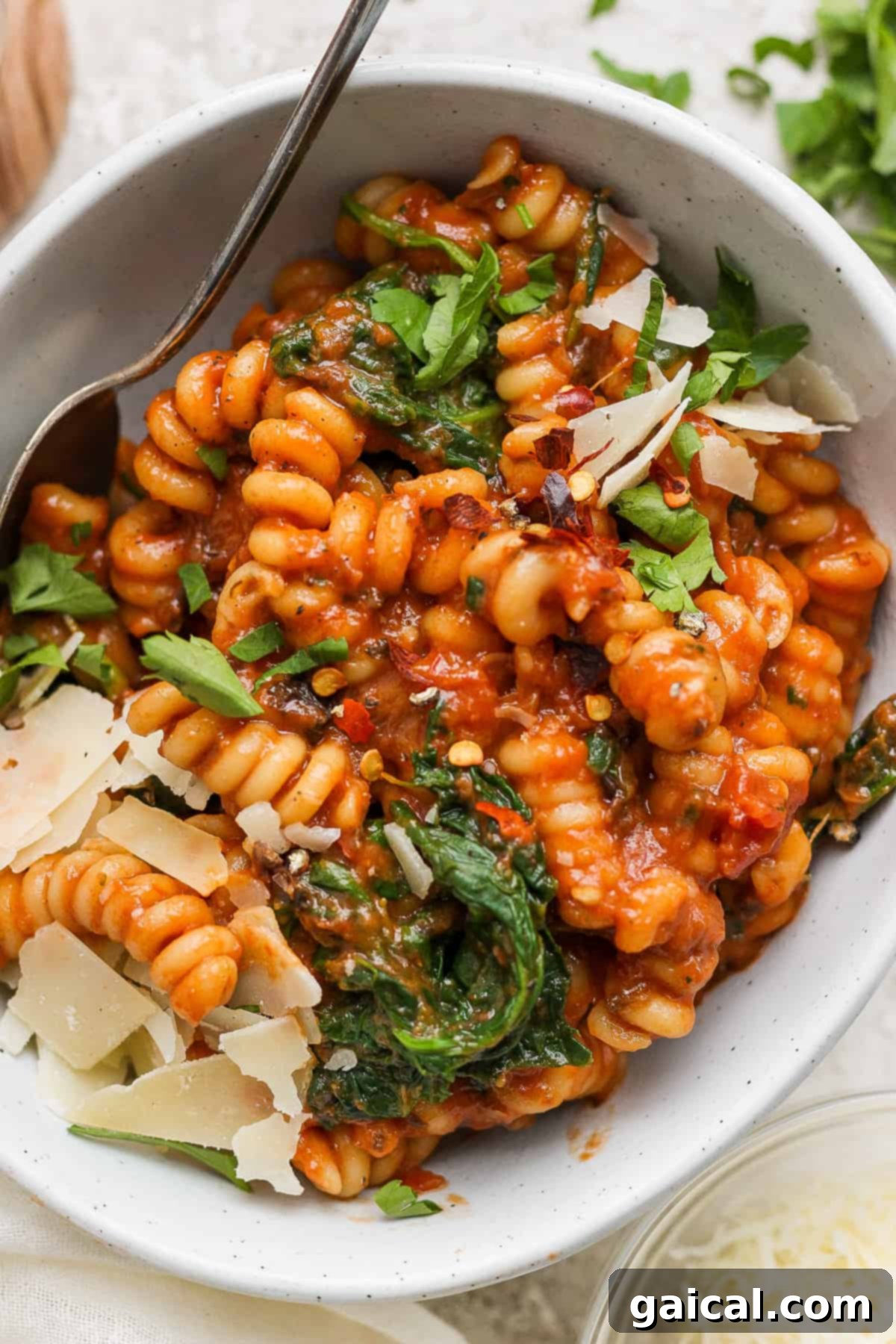 One-Pot Wonder Vodka Pasta 6 A close-up of a beautifully plated bowl of fusilli pasta, generously coated in a vibrant tomato sauce, dotted with green spinach, and crowned with delicate shavings of Parmesan cheese.