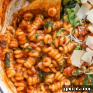One-Pot Wonder Vodka Pasta 7 A close-up image of a vibrant pasta dish featuring a creamy tomato sauce, garnished with fresh spinach and a generous sprinkle of shredded cheese.