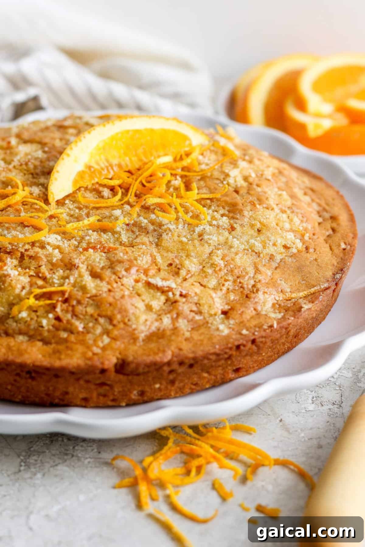 A freshly baked orange olive oil cake garnished with vibrant orange zest, presented beautifully on a white plate, highlighting its golden hue and inviting texture.