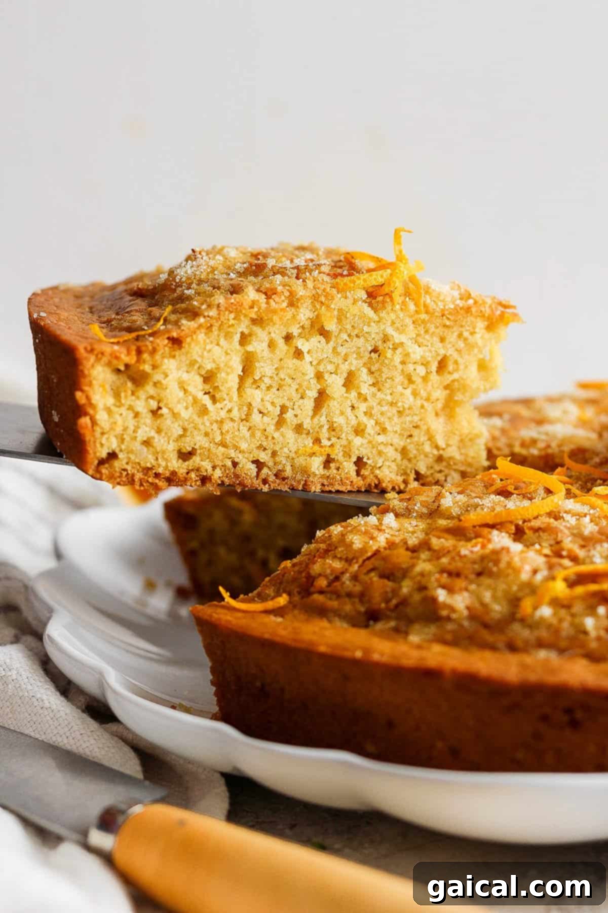 A warm, freshly baked orange olive oil cake with a slice gently lifted out, revealing its moist, tender crumb and the glistening orange zest topping. A truly inviting dessert.