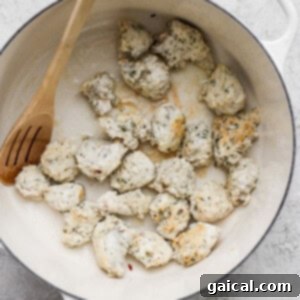 Chicken pieces being cooked in a white pot with a wooden spoon.
