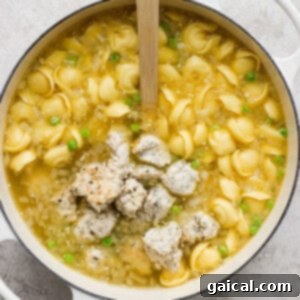 Pot of chicken noodle soup with green peas and a wooden spoon.