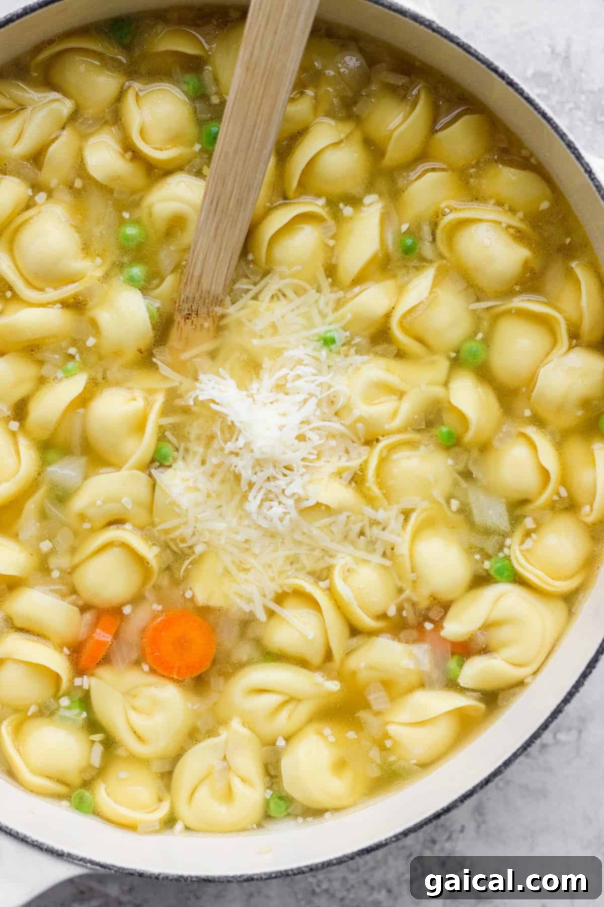 A large pot of vibrant tortellini soup, brimming with carrots and green peas, topped with a generous sprinkle of grated cheese, ready to be served.