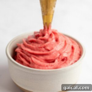 Strawberry Soft Swirl 11 A piping bag dispensing creamy strawberry frosting into a small beige bowl against a white background.