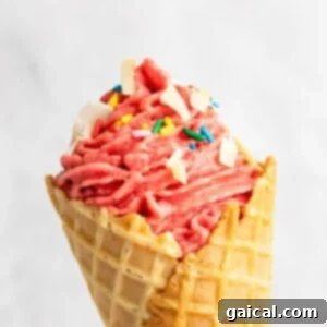 Strawberry Soft Swirl 12 A close-up of a strawberry soft serve ice cream cone topped with sprinkles and white chocolate chunks.