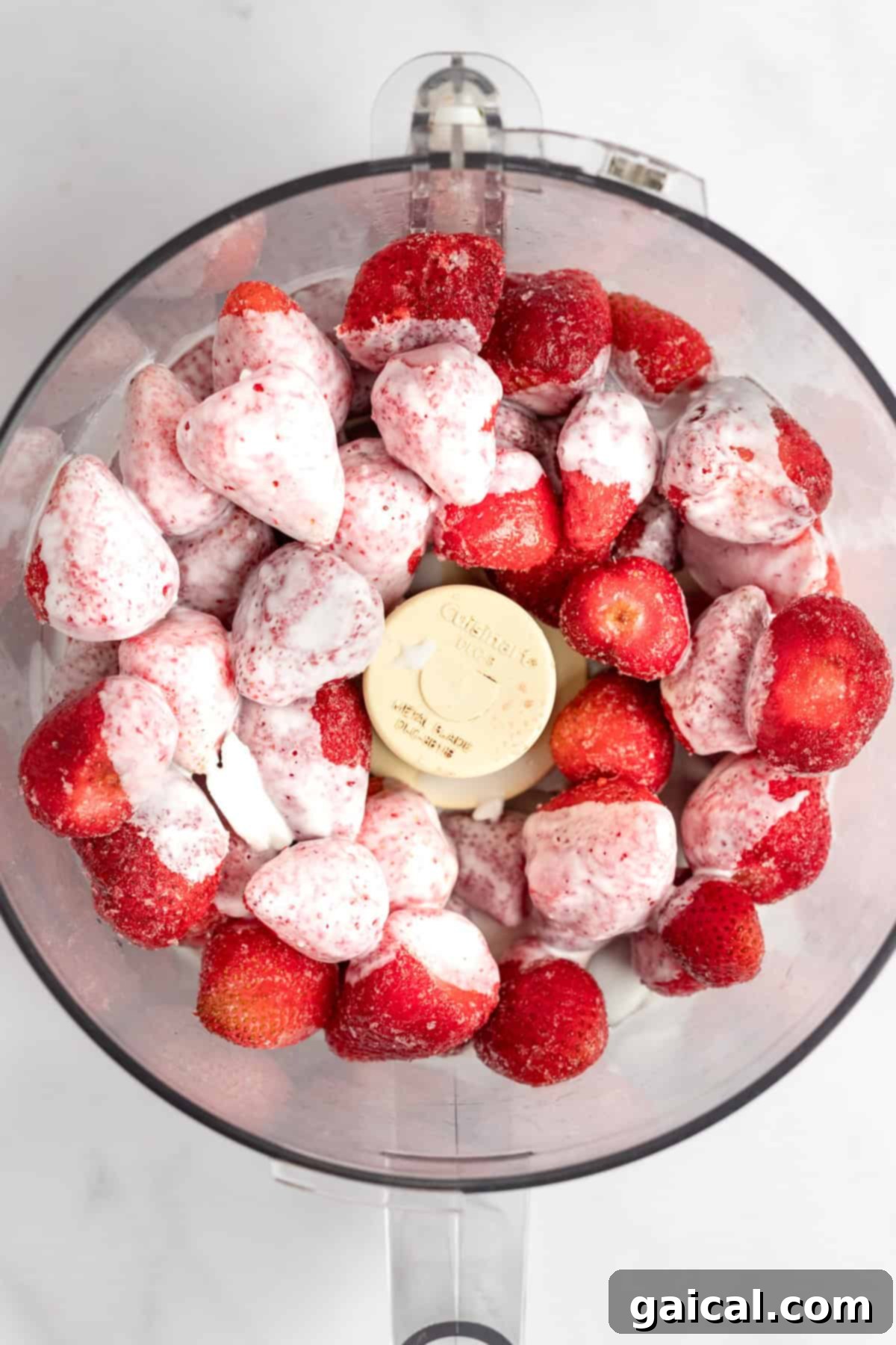 Strawberry Soft Swirl 3 A food processor bowl filled with whole strawberries and scoops of vanilla ice cream, viewed from above.