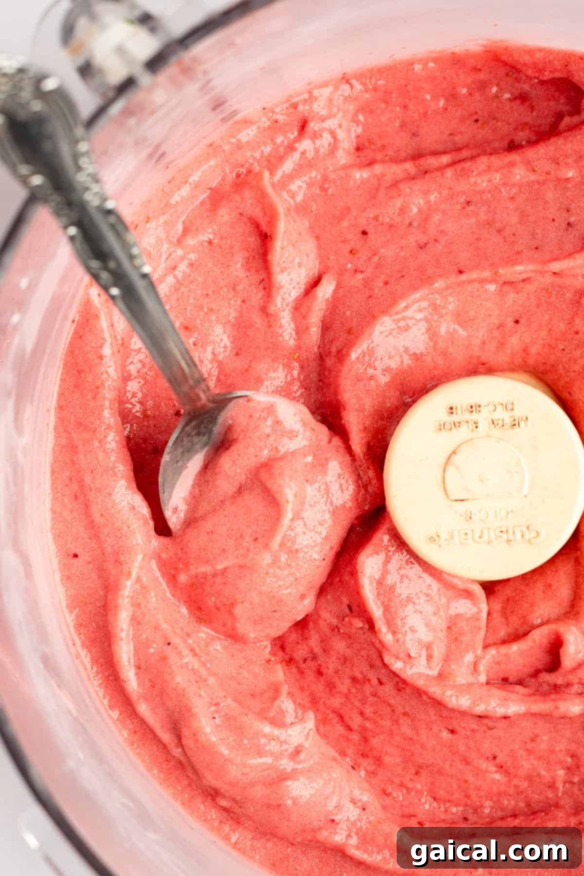 Strawberry Soft Swirl 4 Top-down view of a bowl of fresh strawberry puree with a measuring spoon dipped inside.