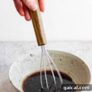A hand using a whisk to combine ingredients for a homemade salad dressing in a ceramic bowl, showing the smooth liquid texture.