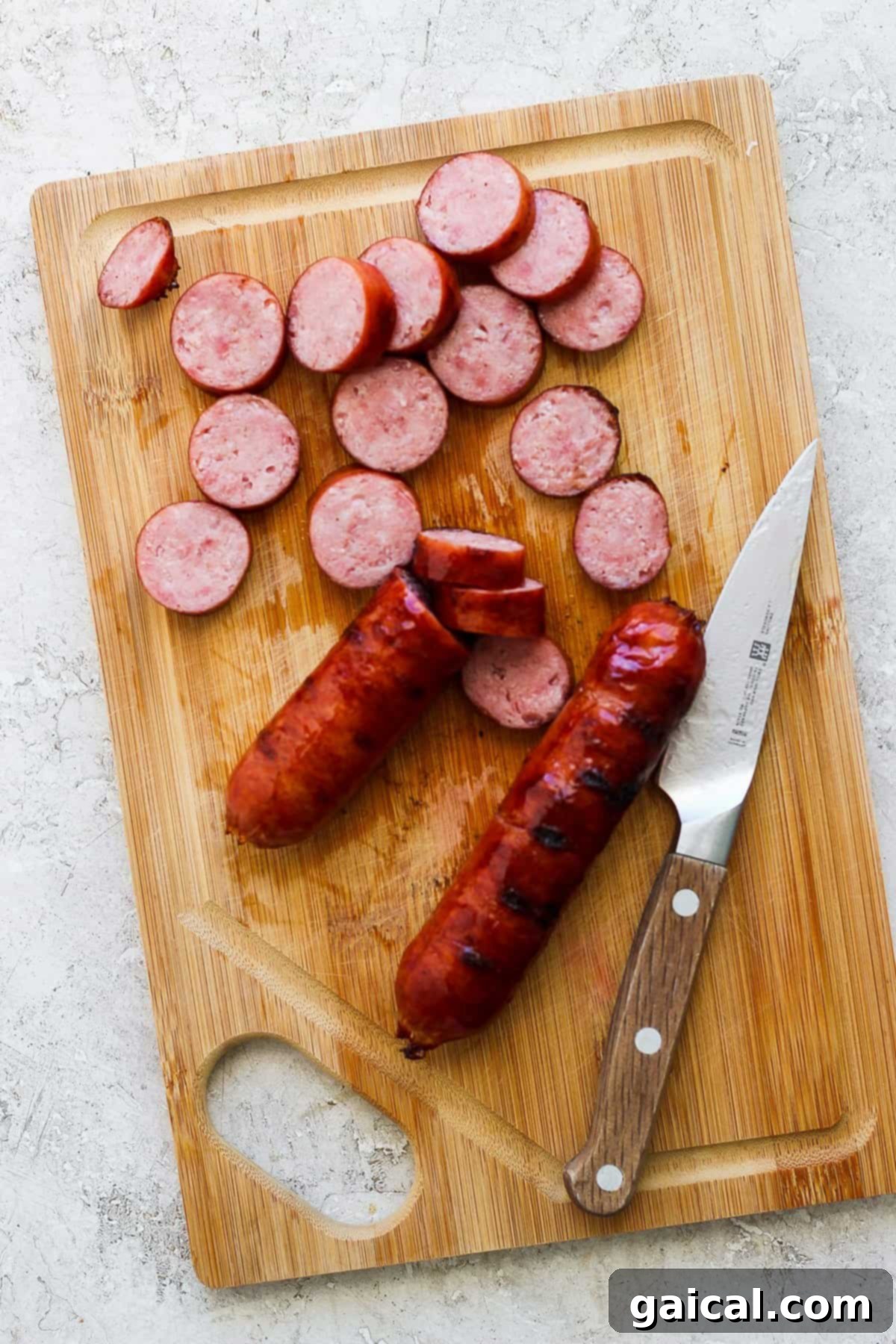 Expertly sliced savory sausage rounds arranged on a rustic wooden cutting board, with a chef's knife beside them, ready for assembly into a delicious meal.