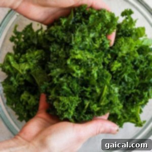 Hands gently massaging fresh kale with olive oil and salt in a glass bowl to soften the leaves for a tender salad.
