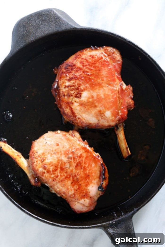 Two perfectly cooked bone-in pork chops resting in a cast iron skillet, golden brown and juicy