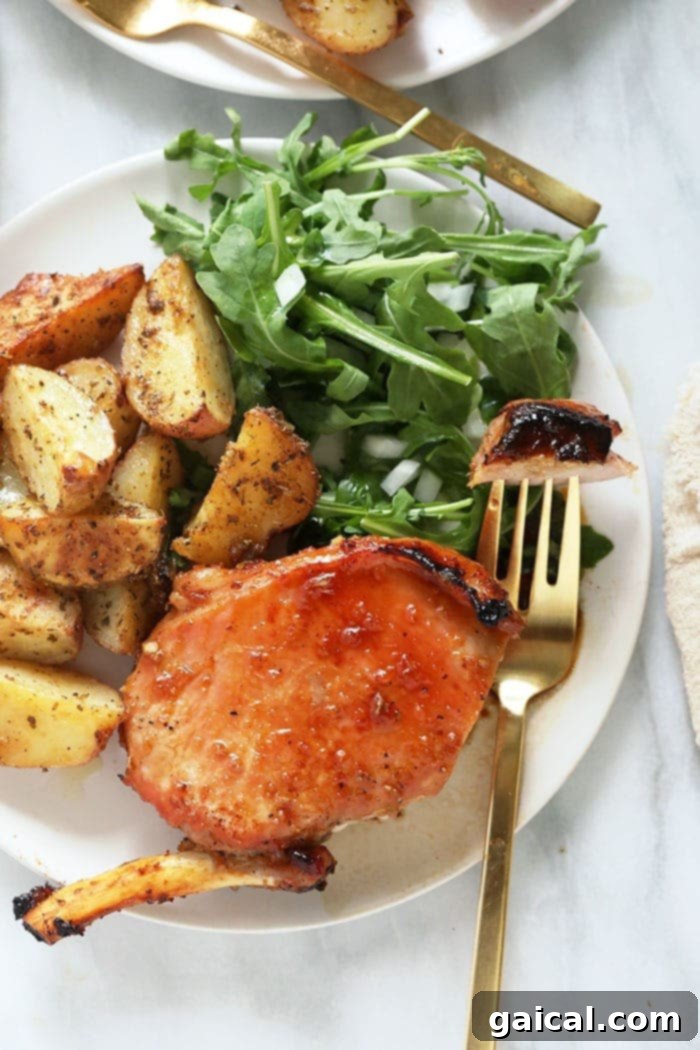 Plated bone-in pork chops with roasted potatoes and green beans, garnished for serving