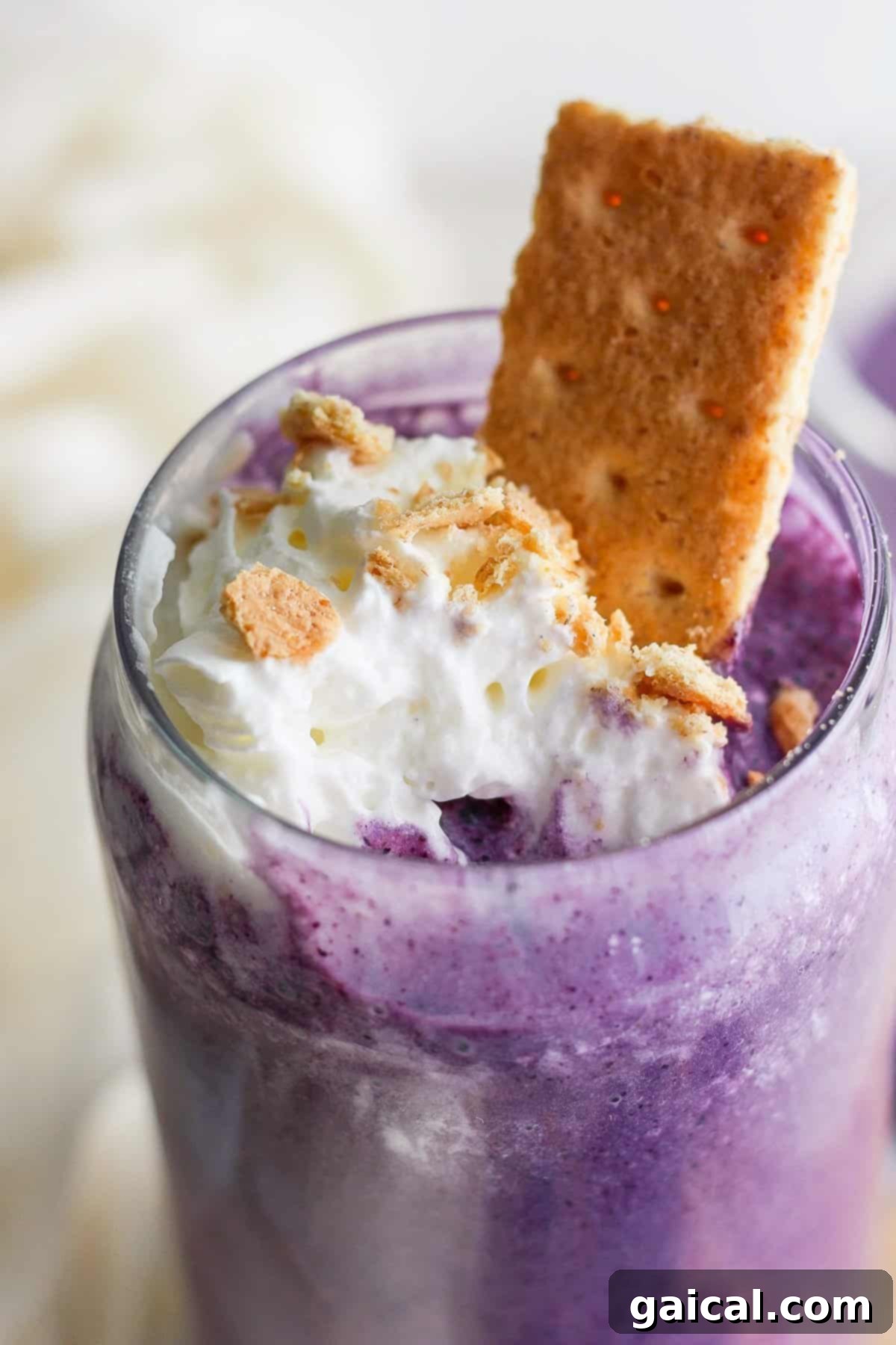 Vibrant Plate Collective 7 A close-up of a purple milkshake topped with whipped cream, crumbled cookies, and a cookie sticking out, served in a clear glass.