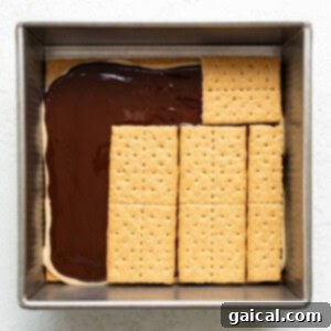A baking dish with a layer of chocolate topped by aligned graham crackers, ready to be frozen for a s'mores dessert.