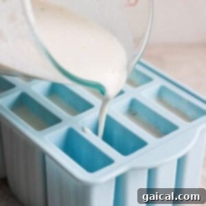 Zesty Coconut Key Lime Frozen Treats 8 Coconut-lime mixture being poured into individual popsicle molds, showing the liquid level.