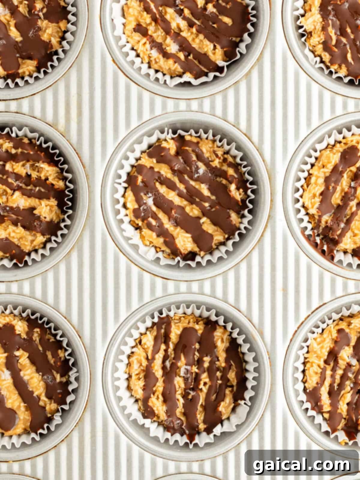 A baking sheet with nine muffin tin liners filled with a mixture topped with drizzled chocolate.