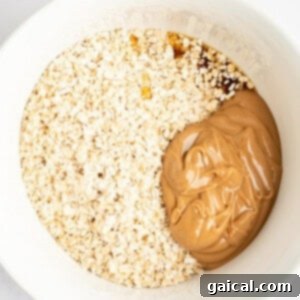A white bowl containing a mixture of oats, peanut butter, and a brown liquid ingredient, possibly honey or syrup, inside.