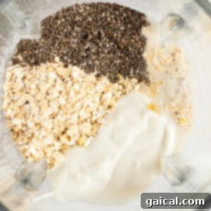 Ingredients including chia seeds, oats, and a creamy liquid mixture in a blender container, viewed from above.