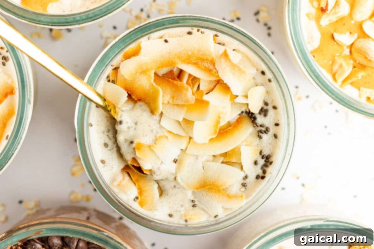 A glass bowl filled with a creamy mixture topped with toasted coconut flakes and chia seeds, with a gold spoon inserted into it. Other similar bowls are partially visible around it.