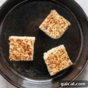 Three toasted Rice Krispie treats in a cast iron skillet on a light textured surface.