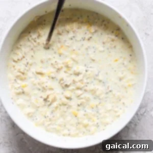 A bowl of oat mixture with chia seeds and grated lemon zest, reminiscent of creamsicle overnight oats, stirred with a spoon.