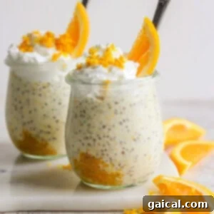 Two glass jars filled with creamy creamsicle overnight oats, topped with whipped cream and orange slices, arranged on a white surface with additional orange wedges nearby.