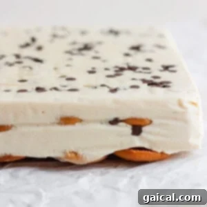Close-up of a layered peanut butter banana ice box cake with a creamy white filling, chocolate chips on top, and a base of cookies, set on crinkled parchment paper.