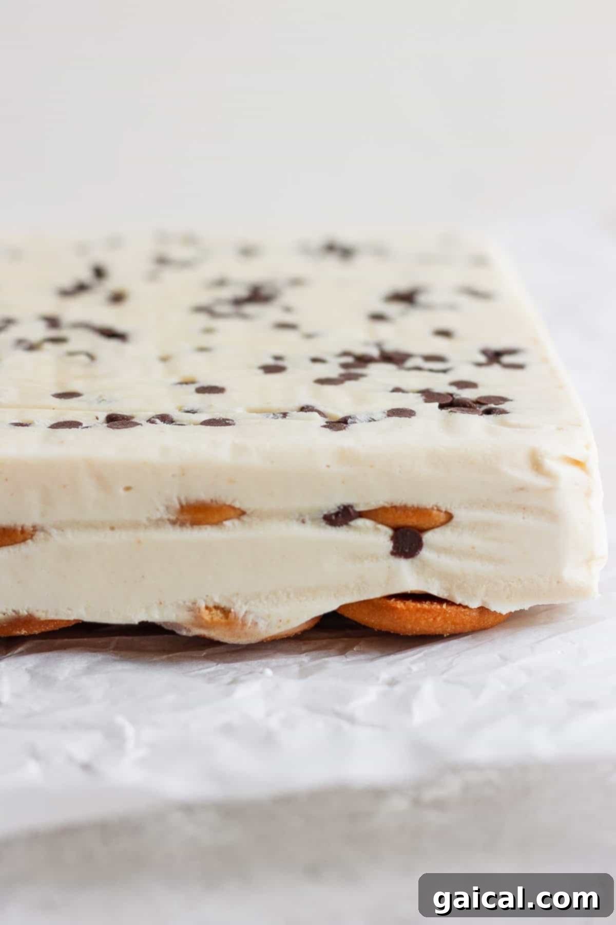 Creamy Peanut Butter Banana No-Bake Delight 4 Close-up of a layered peanut butter banana ice box cake with a creamy white filling, chocolate chips on top, and a base of cookies, set on crinkled parchment paper.