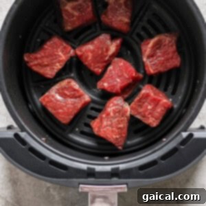 Raw beef pieces arranged in an air fryer basket, ready for cooking.