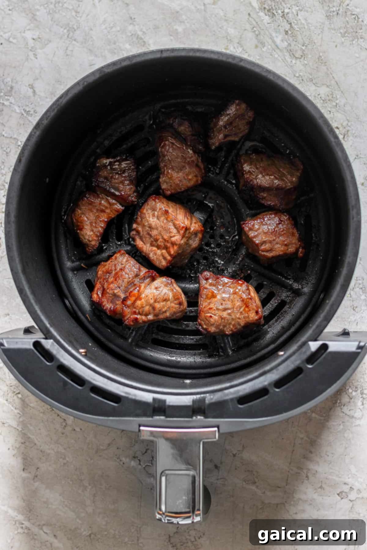 A close-up view of perfectly cooked steak bites resting in an air fryer basket, showing their crispy, golden-brown crust.