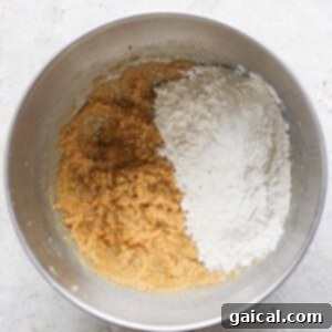 A mixing bowl with brown batter, white flour, and a hint of lemon zest sits on a gray surface, ready for transformation into delicious lemon cookies with cream cheese frosting.