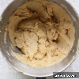 A mixing bowl filled with creamy, beige lemon cookie dough on a textured, light gray surface evokes the promise of sweet treats topped with luscious cream cheese frosting.