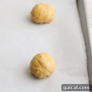 Two balls of lemon cookie dough placed on a parchment-lined baking sheet, destined for a sweet finish with cream cheese frosting.