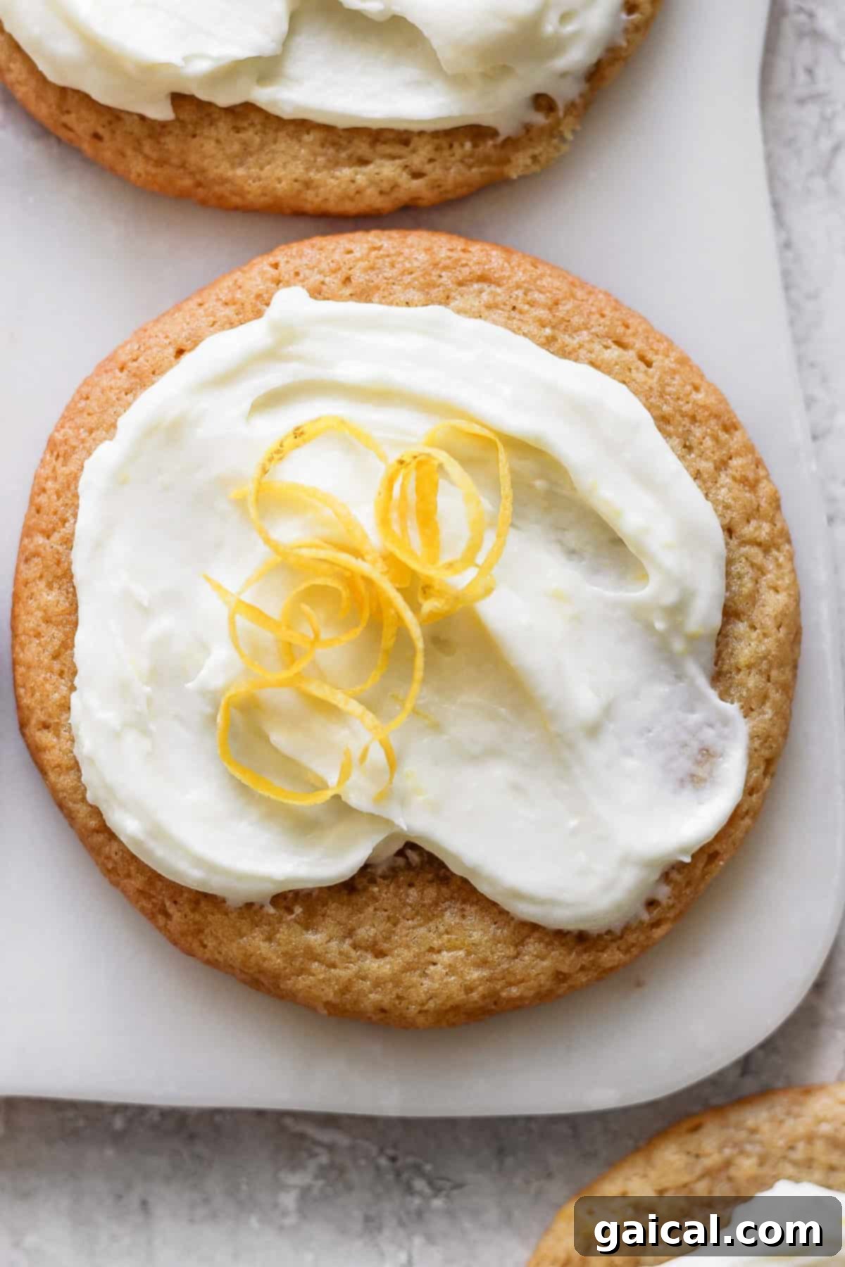 A lemon cookie adorned with cream cheese frosting and garnished with a twist of lemon peel.