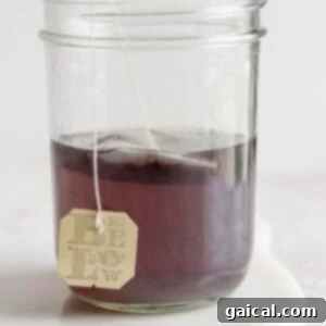 A clear jar filled with water and a tea bag infusing, turning the water purple.