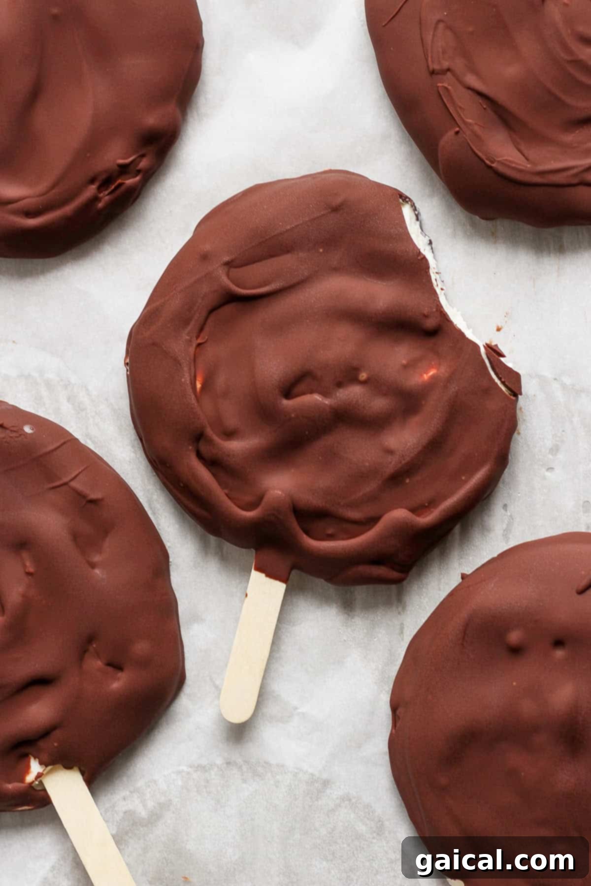 Homemade Dilly Delights 2 Chocolate-covered ice cream bars on sticks, viewed from above, with one bar having a bite taken out of it.