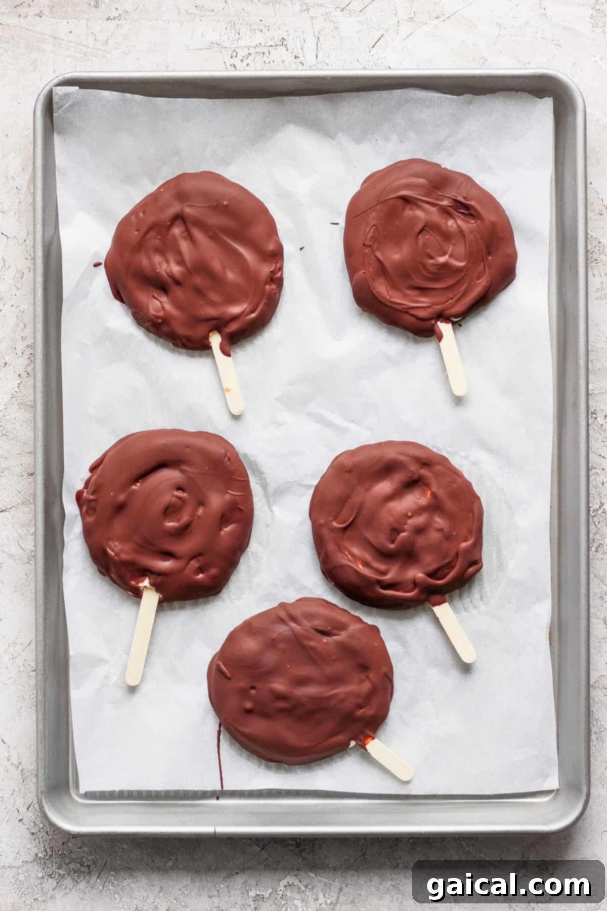 Homemade Dilly Delights 4 Five chocolate-covered treats on wooden sticks rest on a parchment-lined baking sheet.