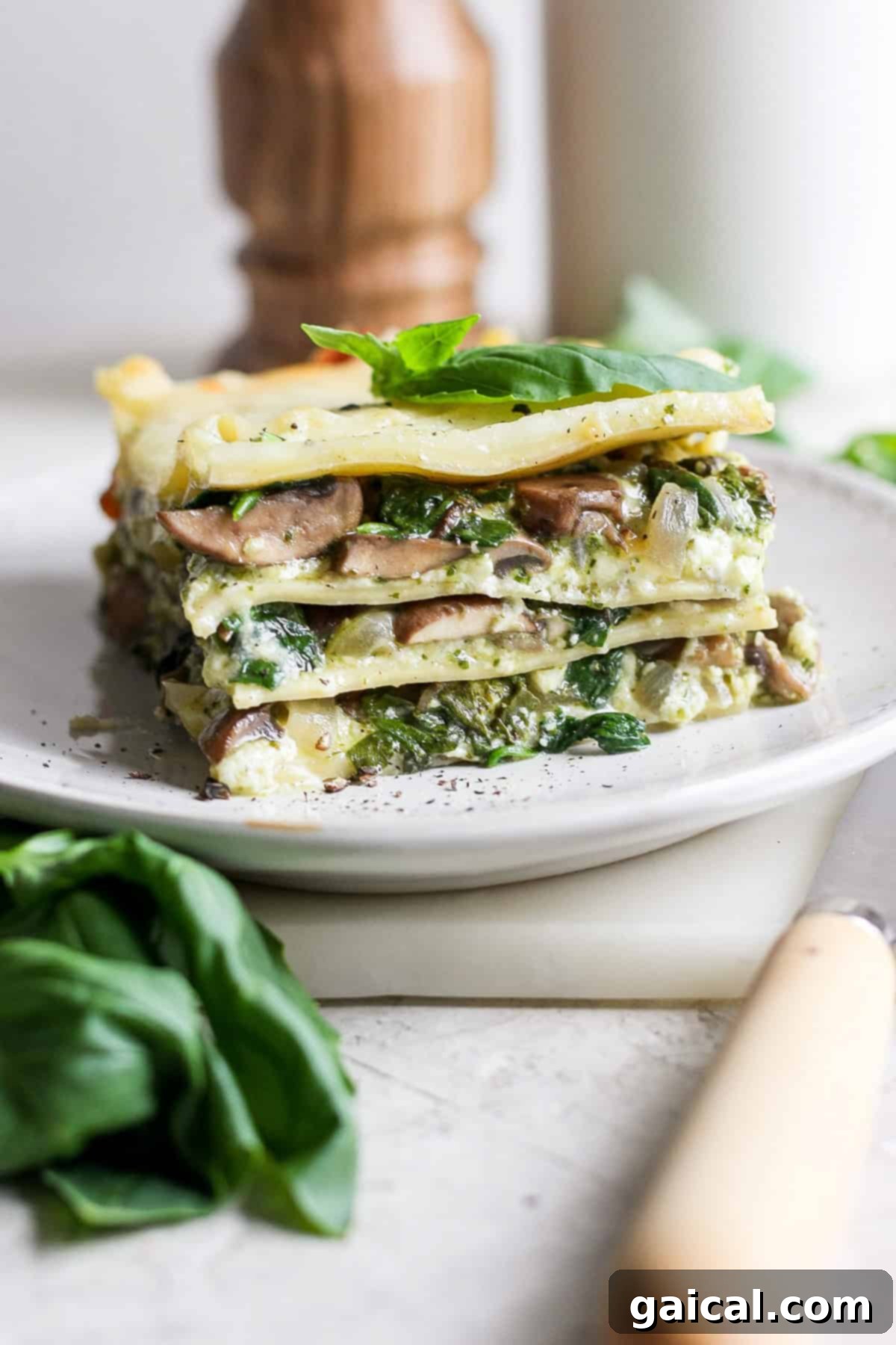 Rustic Pesto Lasagna 2 A perfectly portioned slice of vibrant vegetarian pesto lasagna on a white plate, showcasing its distinct layers of pasta, bright green pesto, creamy cheese, sautéed spinach, and tender mushrooms, elegantly garnished with fresh basil leaves.