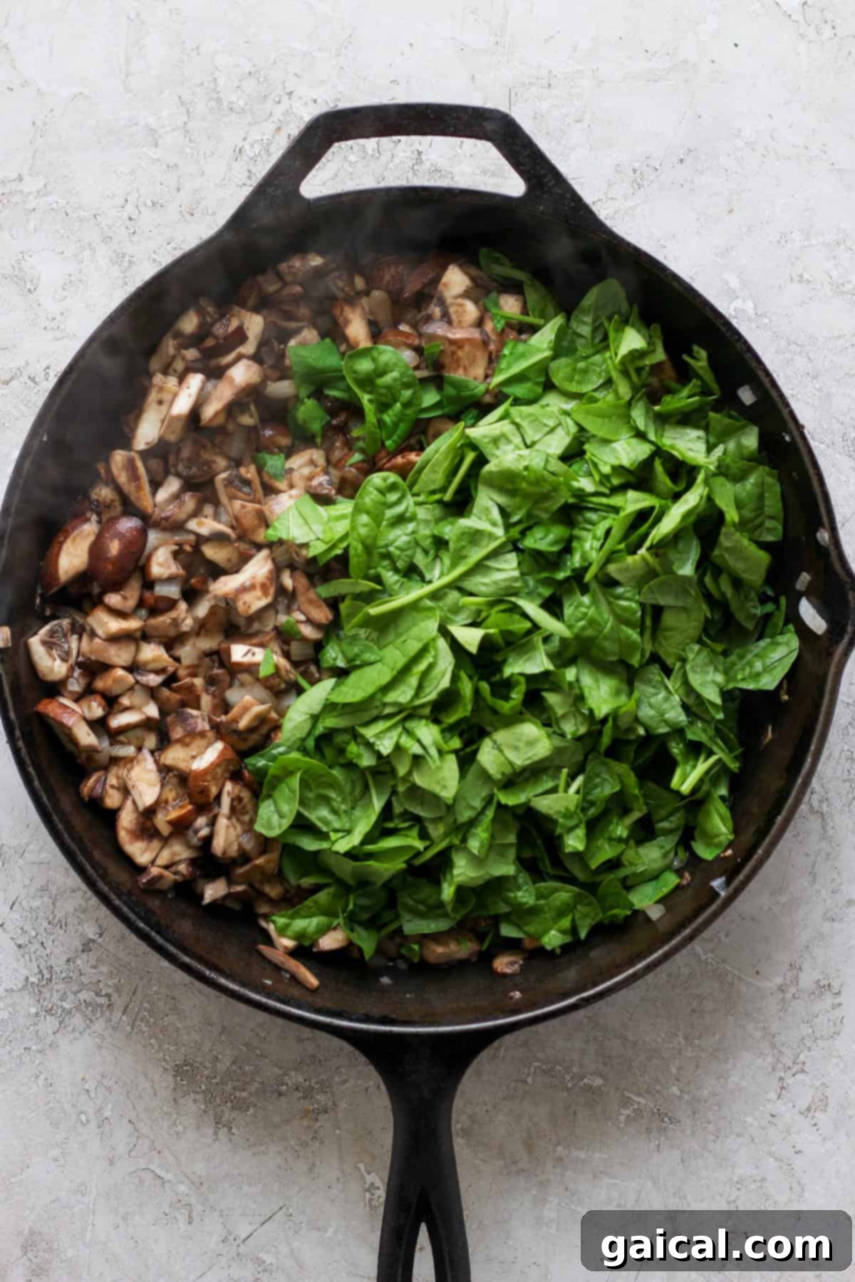 Rustic Pesto Lasagna 3 A rustic cast-iron skillet divided, with one side brimming with freshly chopped bella mushrooms and the other side piled high with vibrant, fresh spinach leaves, all set on a light-colored, textured kitchen surface.