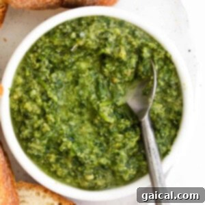 Rustic Pesto Lasagna 6 A rustic wooden bowl filled with vibrant green homemade pesto, accompanied by crusty bread slices and a spoon, all resting on a textured surface.