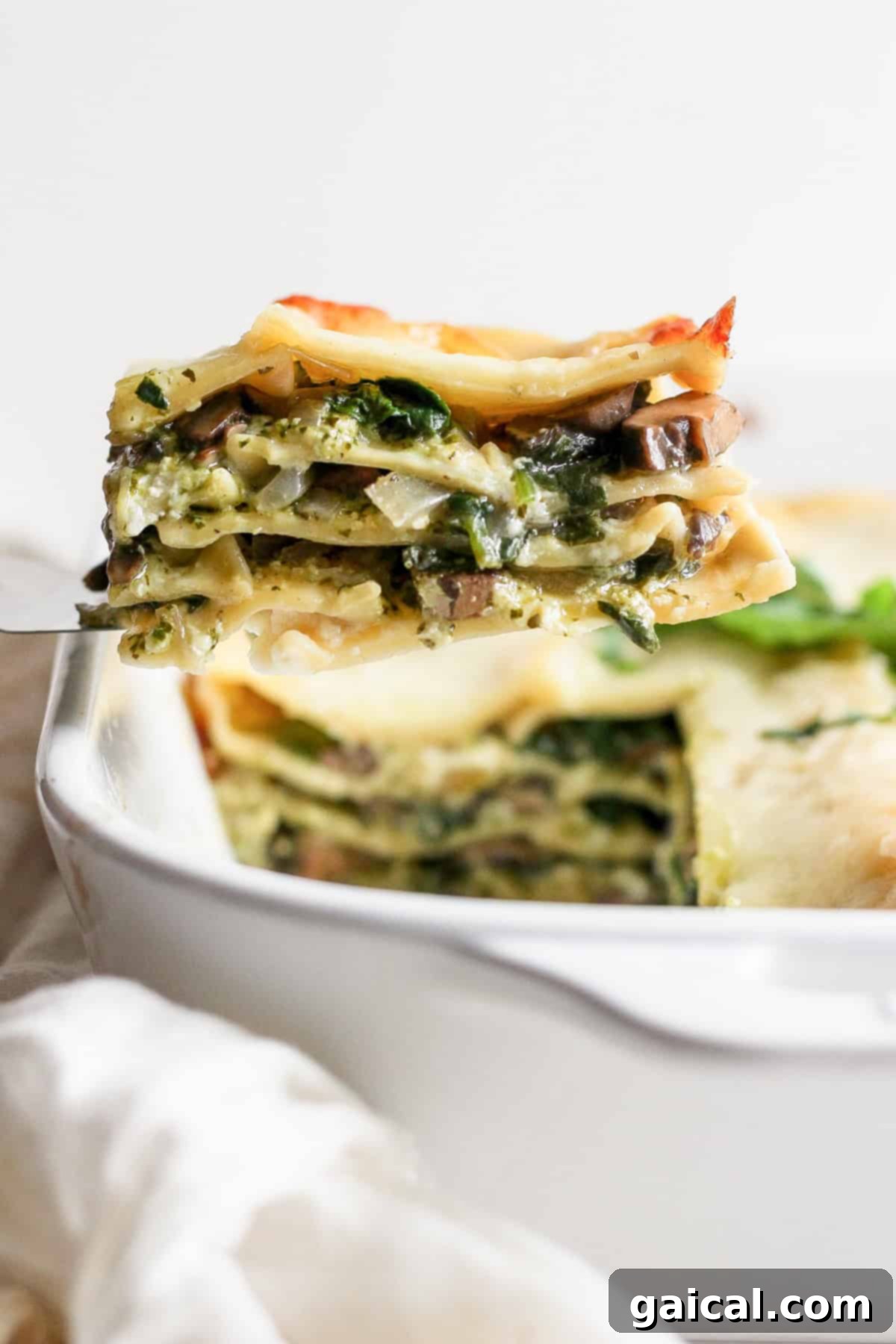 Rustic Pesto Lasagna 7 A close-up shot of a perfect slice of vegetable lasagna being carefully lifted from a white baking dish, revealing distinct, creamy layers of pasta, vegetables, and melted cheese, emphasizing its delicious texture.