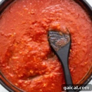 Rich tomato sauce bubbling in a pan with a wooden spoon, showcasing the sauce preparation step.