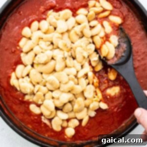 A skillet filled with creamy butter beans immersed in a rich tomato sauce, simmering on the stove.