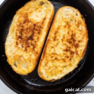 Two slices of hearty bread perfectly toasted to a golden brown in a cast iron skillet, ready for topping.