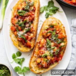 Two slices of gourmet beans on toast, topped with a rich bean mixture, grated parmesan, and fresh gremolata.