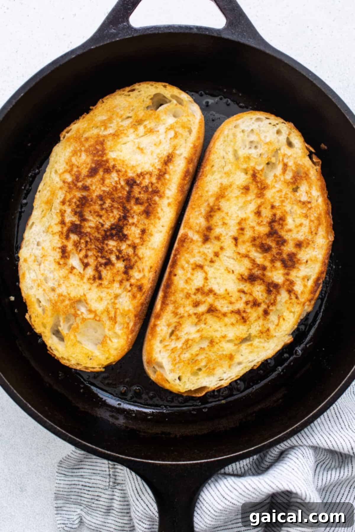 Two slices of golden-brown toast, glistening with butter or oil, in a hot cast iron skillet, ready to be topped.