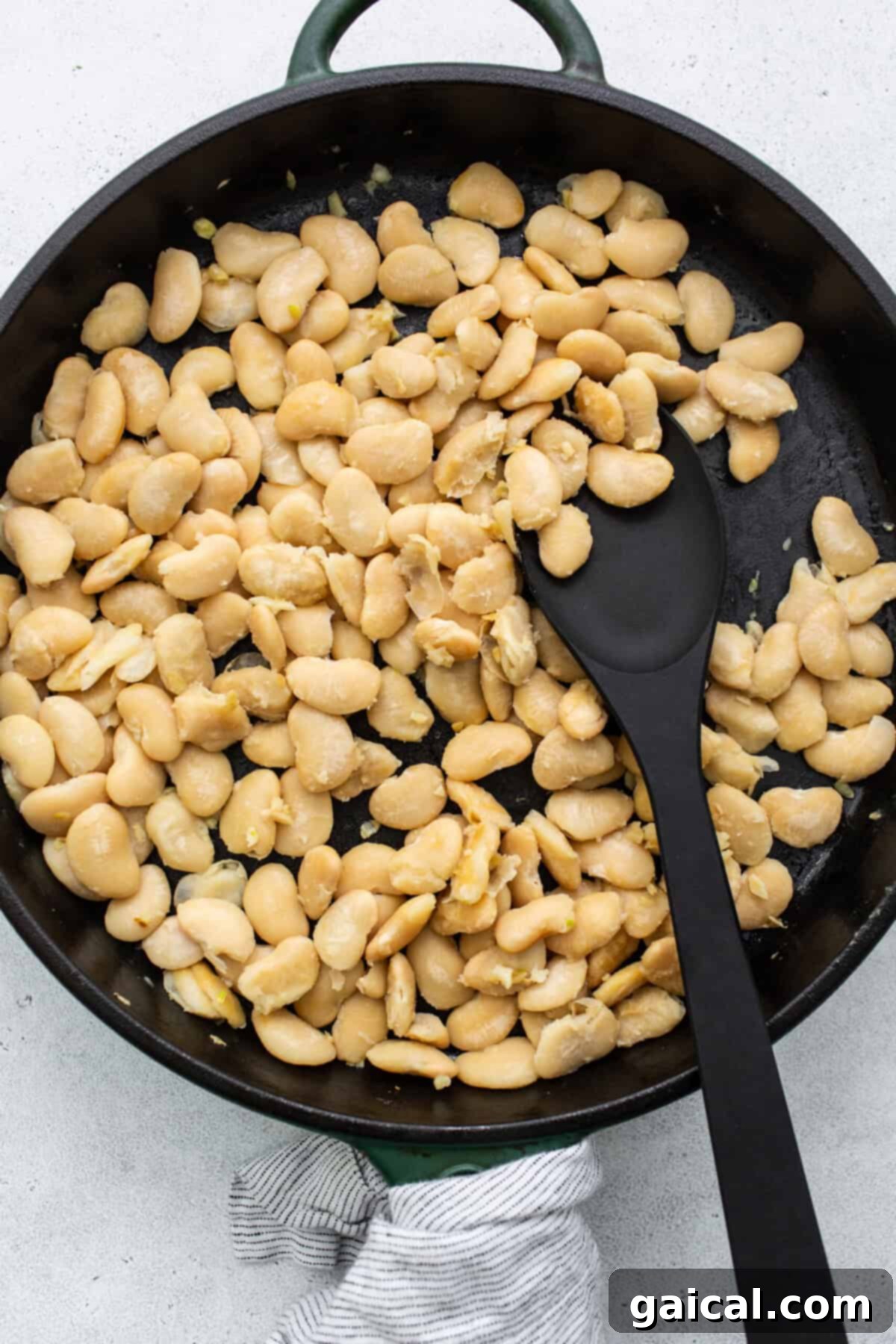 Hearty white butter beans sizzling gently in a frying pan alongside garlic, ready to be coated in lemon juice and pepper.