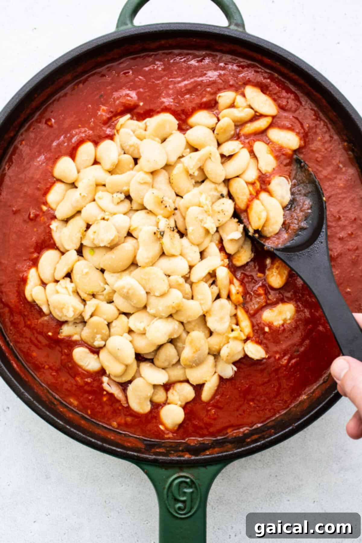 A close-up view of a skillet filled with a thick, rich butter bean and tomato sauce, simmering gently on the stovetop, ready to be served.