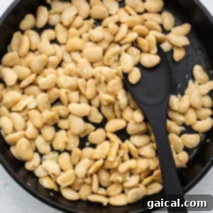 White beans in a frying pan with a black spatula, illustrating the first step of preparing the beans.